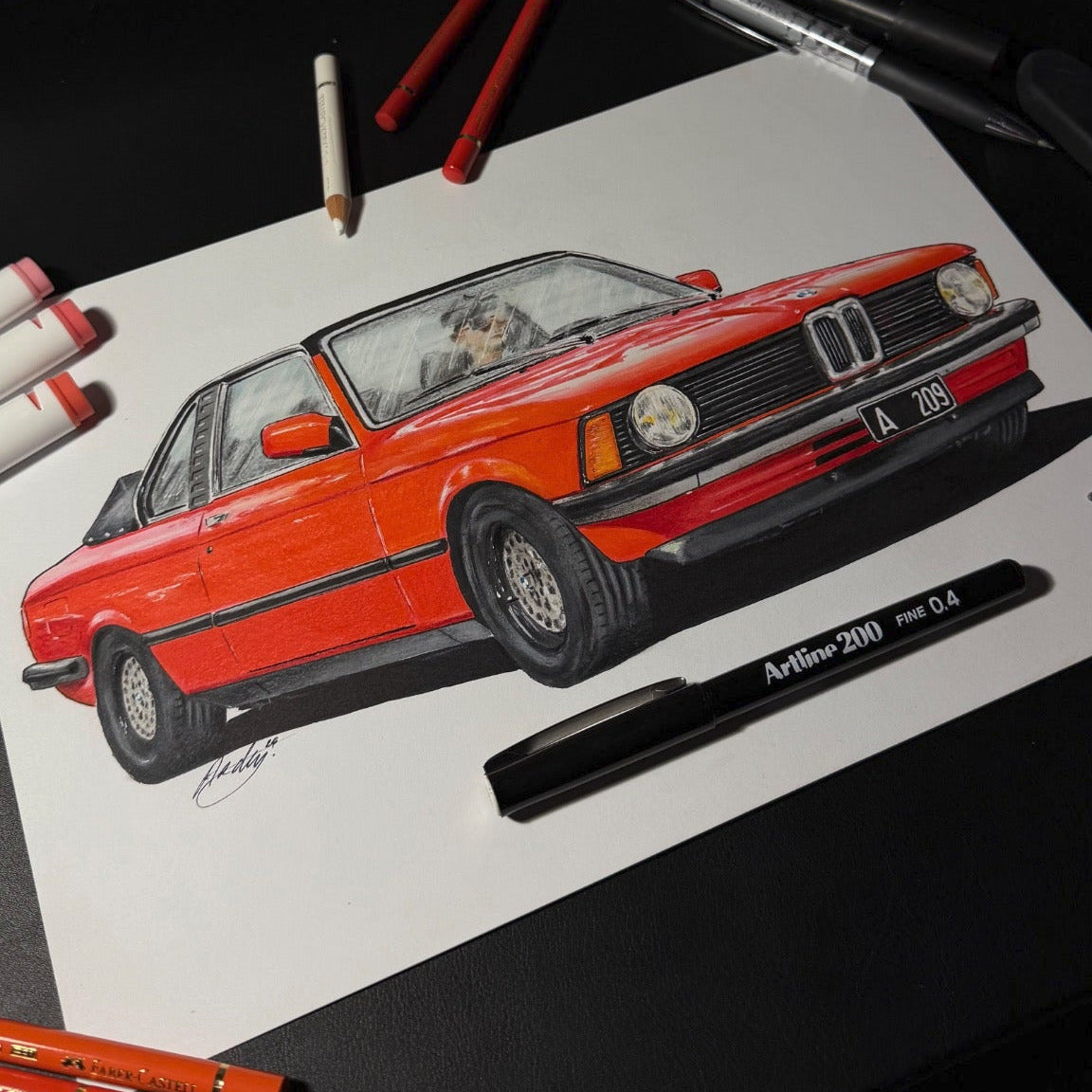 Colorful drawing of a red car on paper with art supplies around