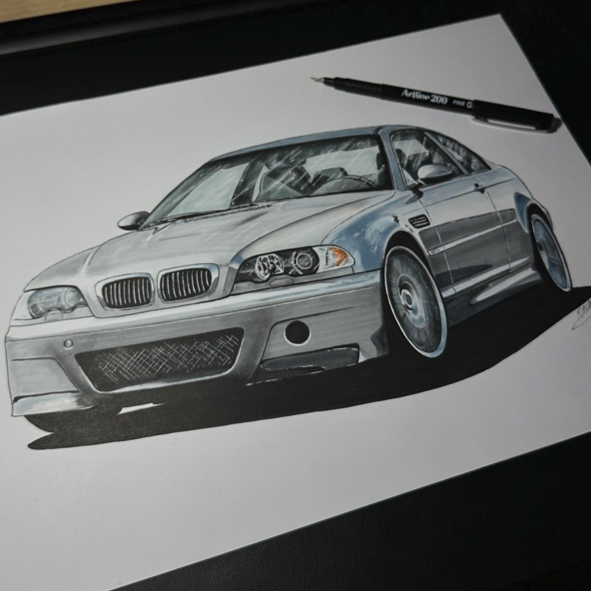 Car drawing on a piece of paper with a pen next to it, and model cars in the background.