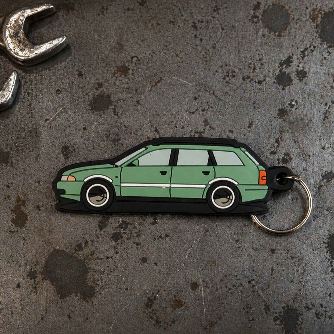 Green car-shaped keychain on a textured metal surface with wrenches.