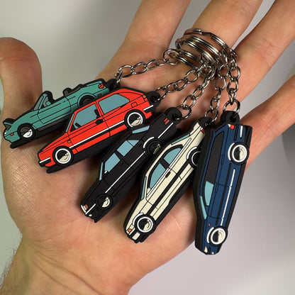 Hand holding multiple car-shaped keychains on a plain background