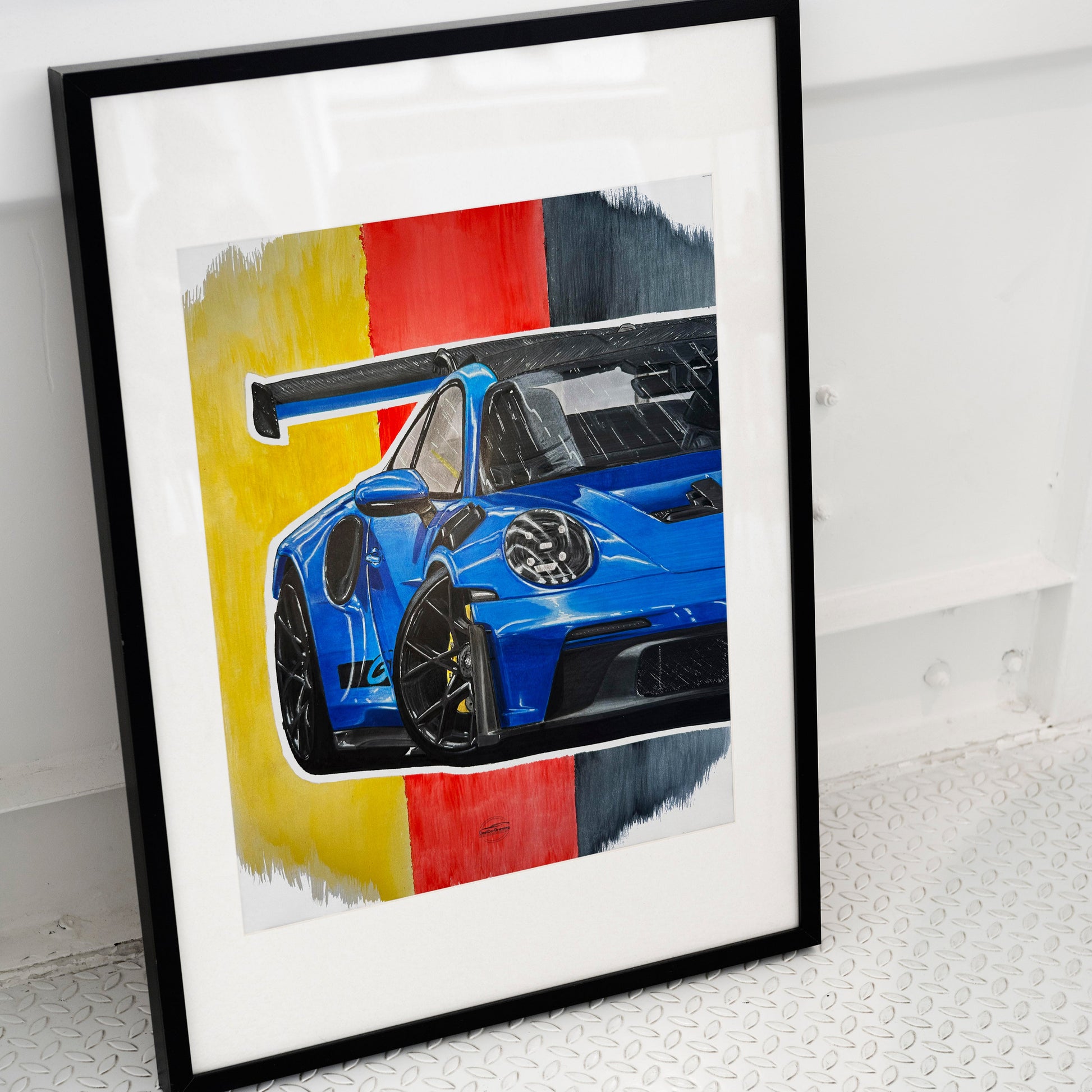 Framed artwork of a blue Porsche GT3RS placed on ground.