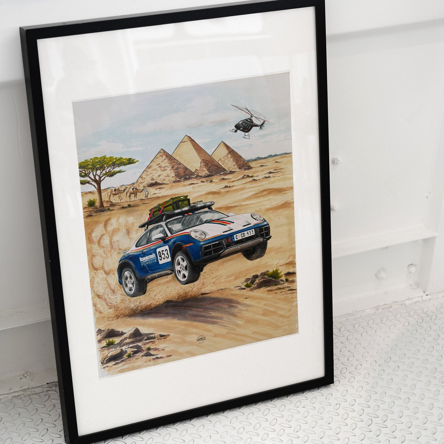 Framed artwork of a Porsche 911 Dakar car in a desert with pyramids and a helicopter.
