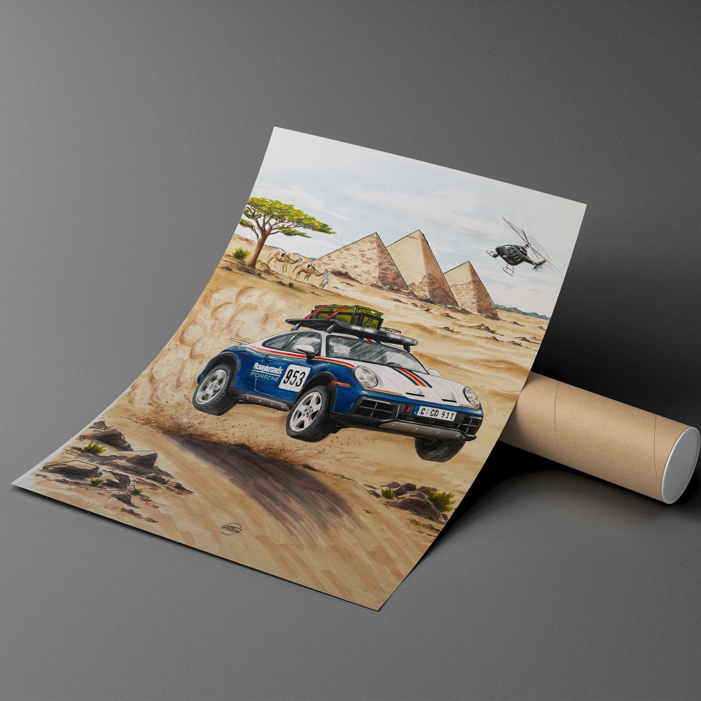 Rolled-up poster of a Porsche Dakar 911 car on a dirt road with pyramids in the background, displayed on a gray surface.